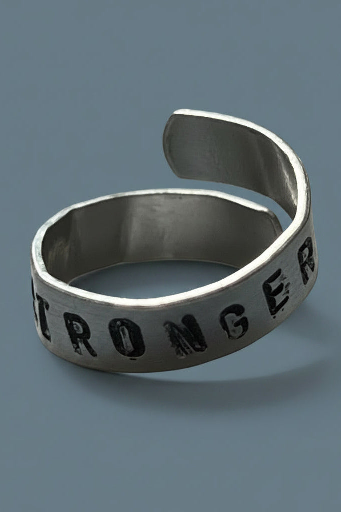 Silver color ring with 'I AM STRONGER' engraving on a gray surface.