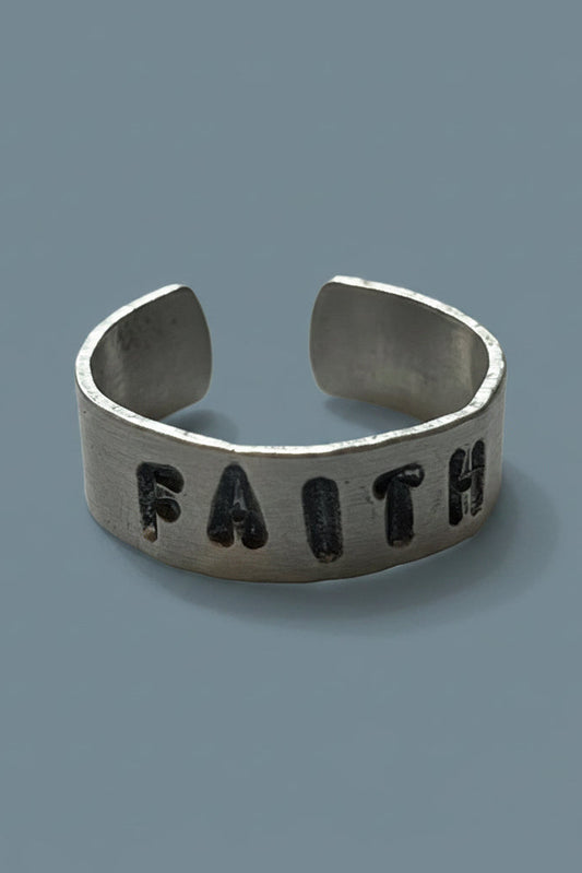 Silver color ring with 'FAITH' engraved by hand stamping on a light gray background.