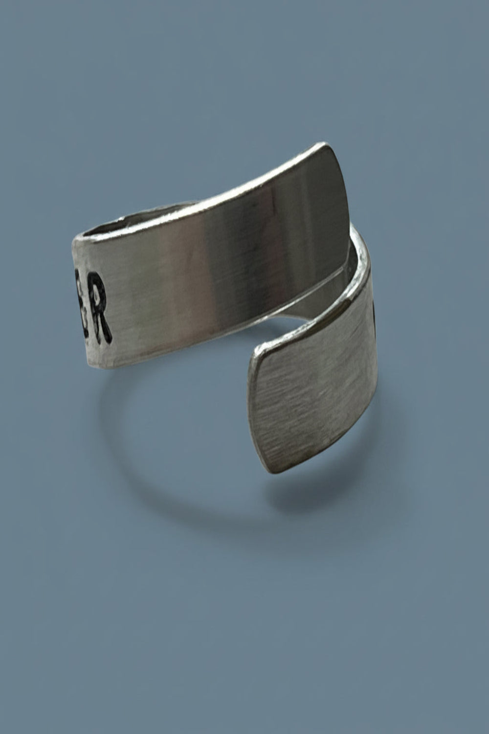 Silver color ring with text "I AM STRONGER" hand stamped.  Cuff ring is on a light gray background