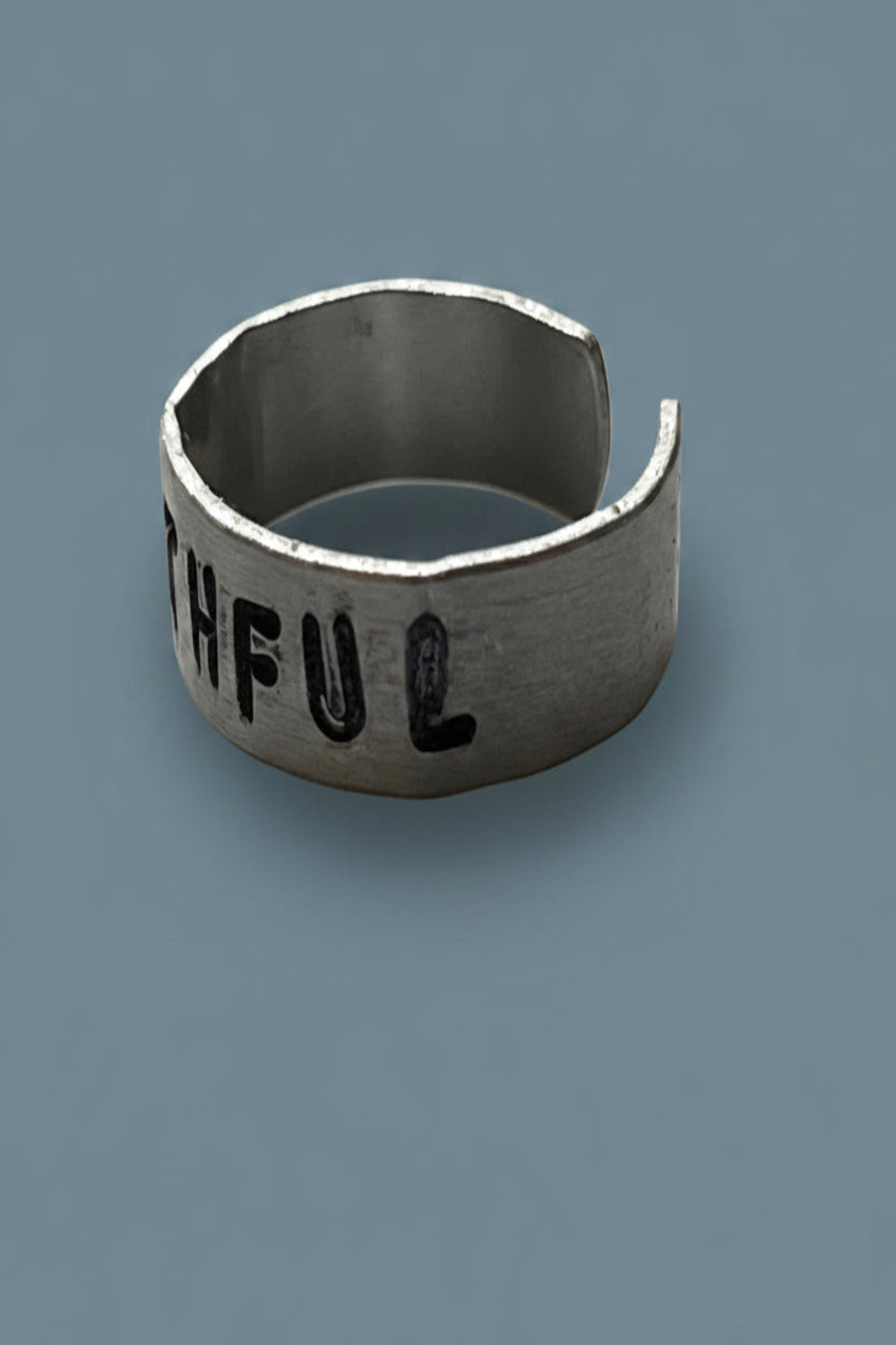 Silver colored cuff ring with 'GRATEFUL' engraving on a gray background