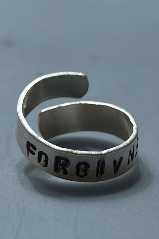 Silver color ring with engraved text that says "FORGIVENESS" on a gray background.