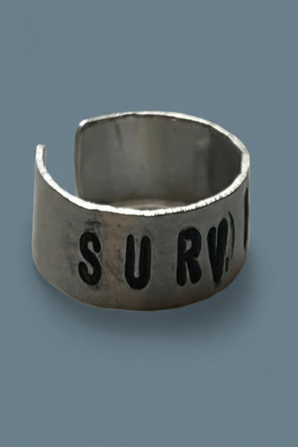 Silver colored ring with 'SURVIVOR' engraved on a blue background.
