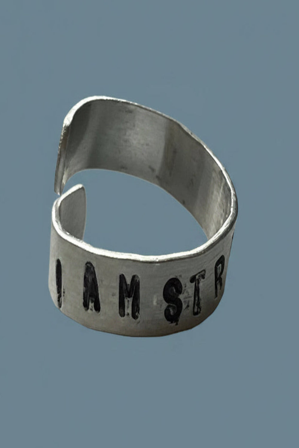 Silver color ring with 'I AM STRONGER' engraved on a blue background.
