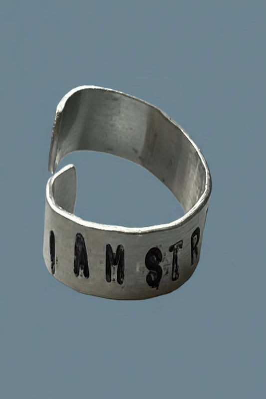 Silver color ring with 'I AM STRONGER' engraved on a blue background.
