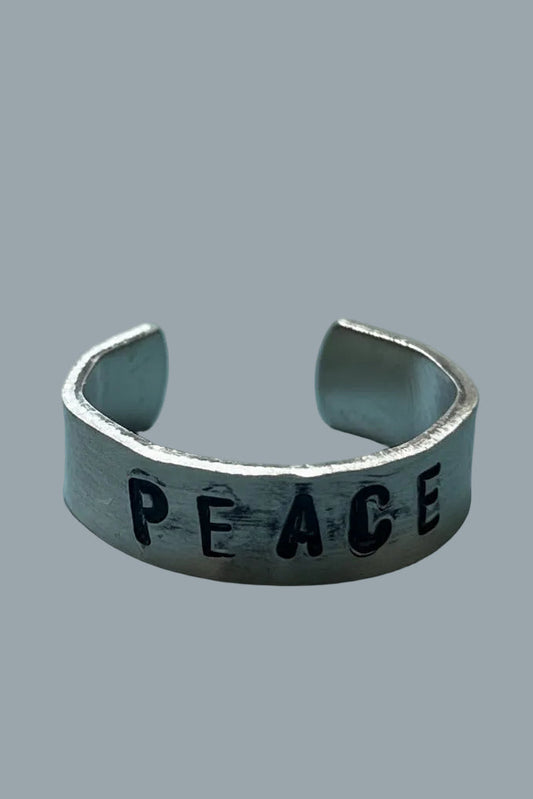 Silver color ring with 'PEACE' engraving done by hand stamping on a gray background.