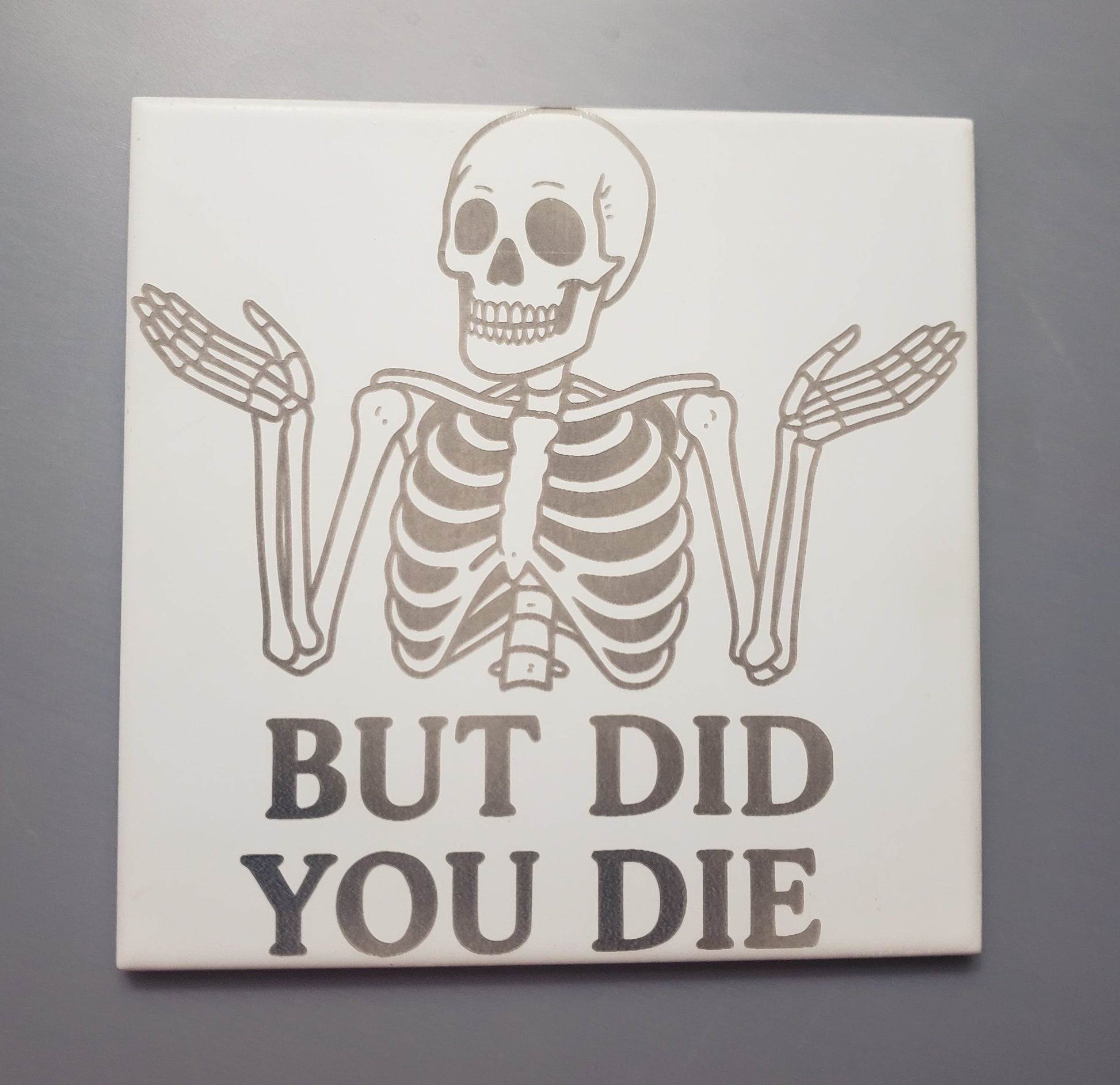 Ceramic tile measuring 6"x6" featuring a shrugging skeleton asking "but did you die" 