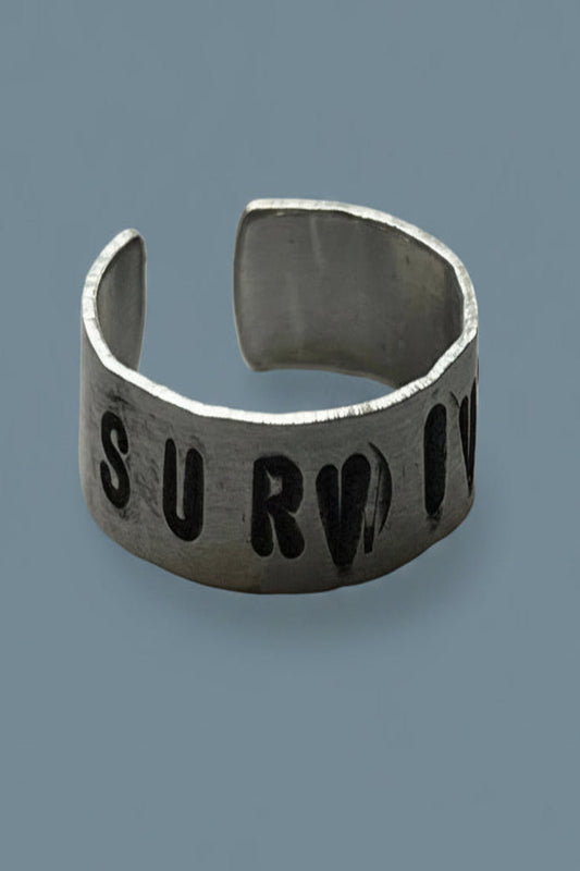 Silver color ring with 'SURVIVOR' engraved on a gray background