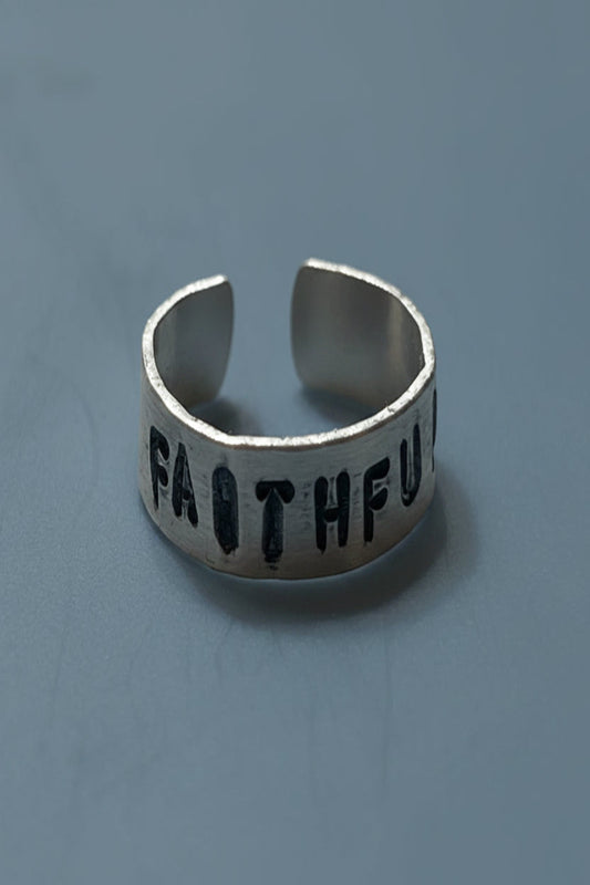 Silver colored ring with 'FAITHFUL' hand stamped engraved on a light gray background