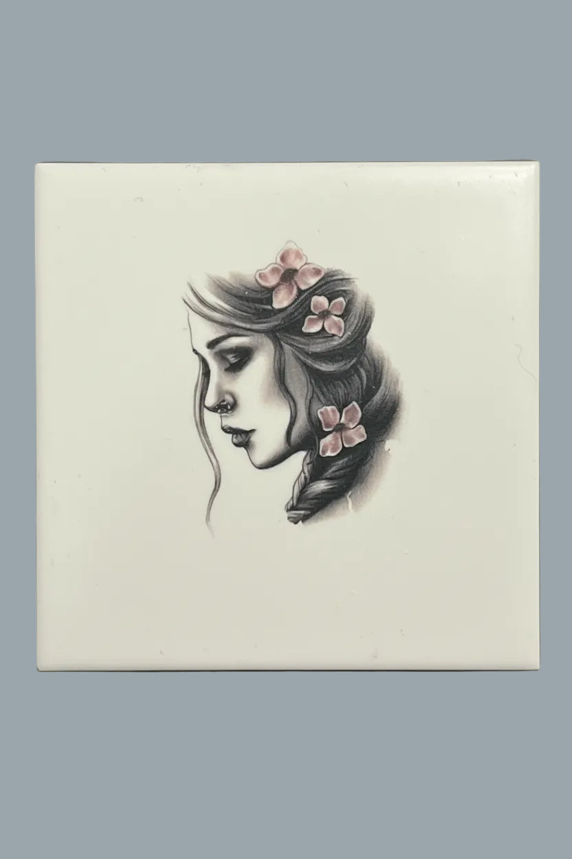 A square ceramic tile featuring a black and white sketch of a woman's profile with pink flowers in her hair.