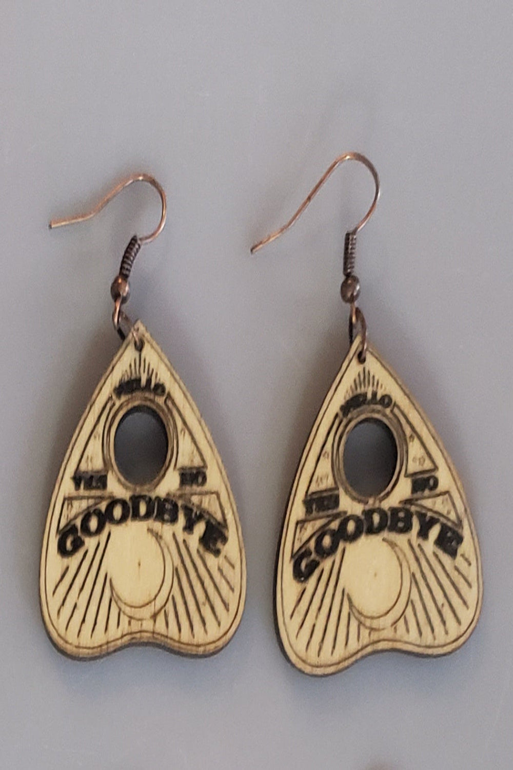 Planchette handle heart-shaped earrings with 'Goodbye' text etched into wood.