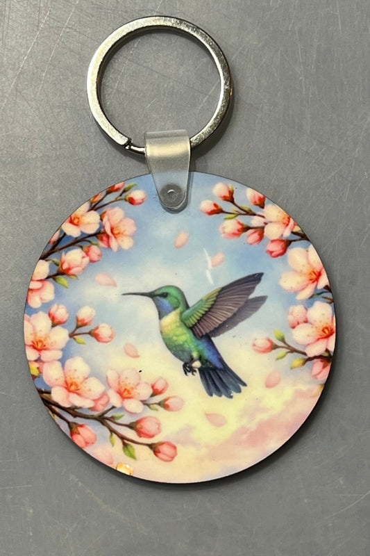 A hummingbird in flight amongst cherry blossoms.  2 1/2" Round key chain.