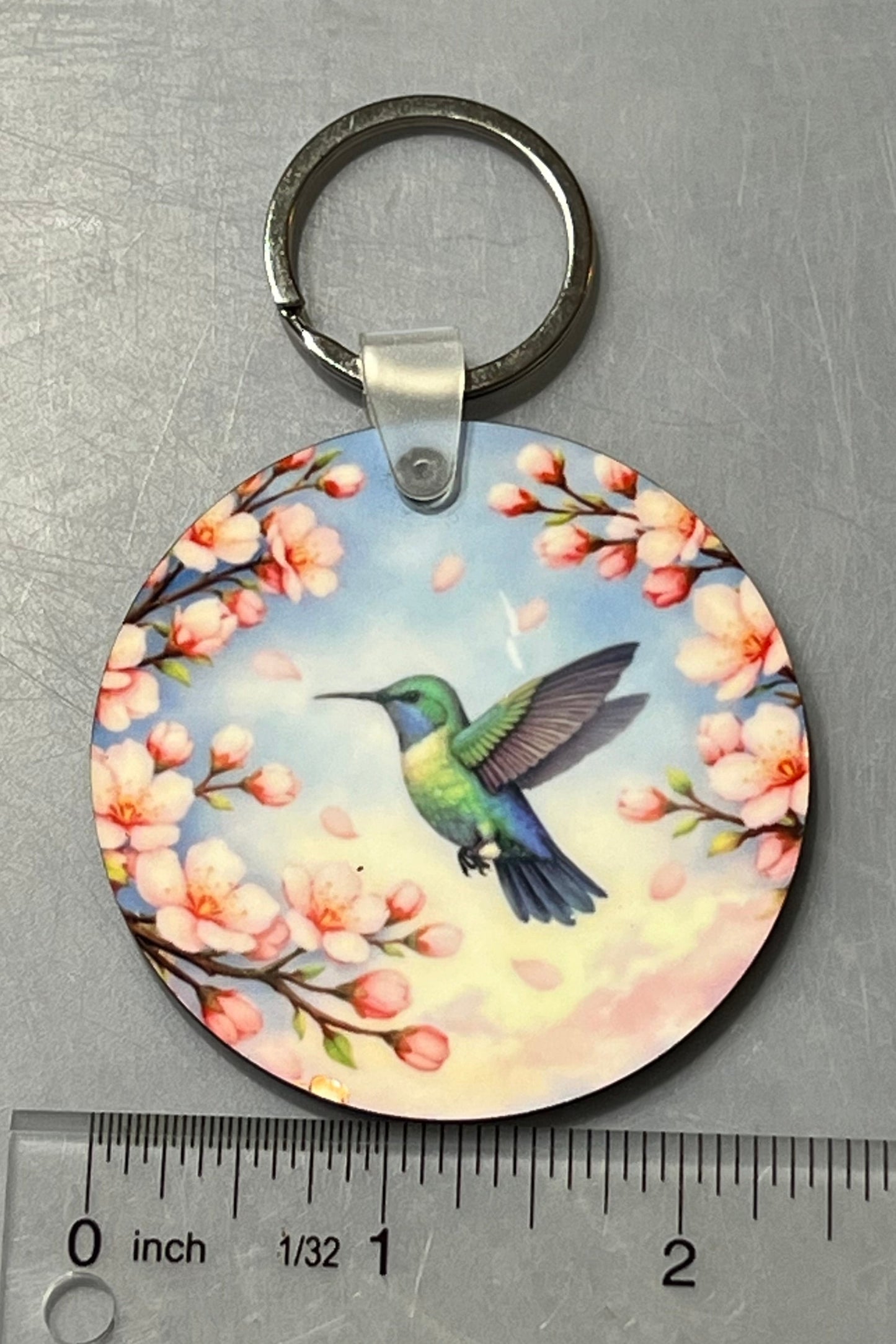 A hummingbird in flight amongst cherry blossoms.  2 1/2" Round key chain. With ruler shown for scale. 