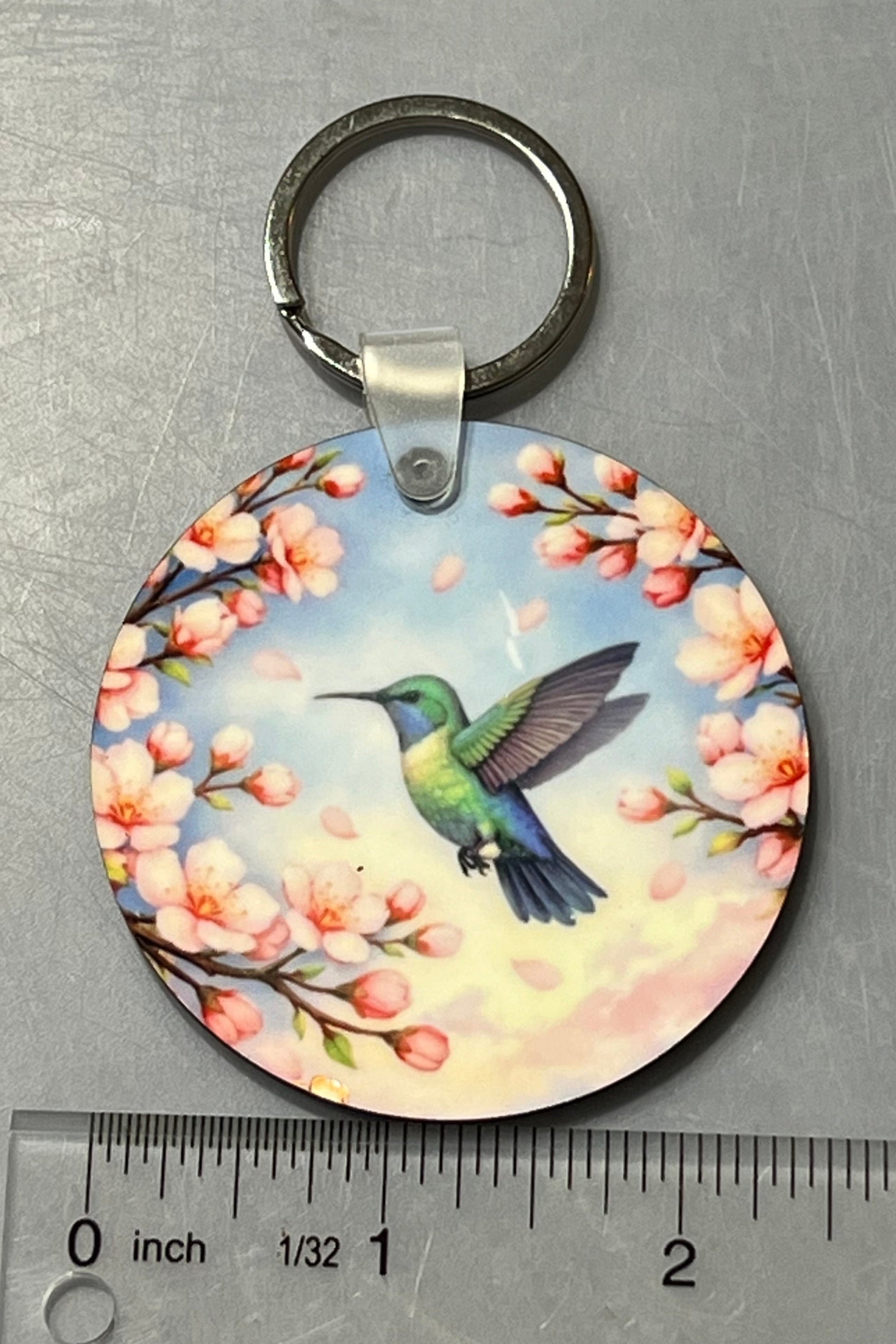 A hummingbird in flight amongst cherry blossoms.  2 1/2" Round key chain. With ruler shown for scale. 