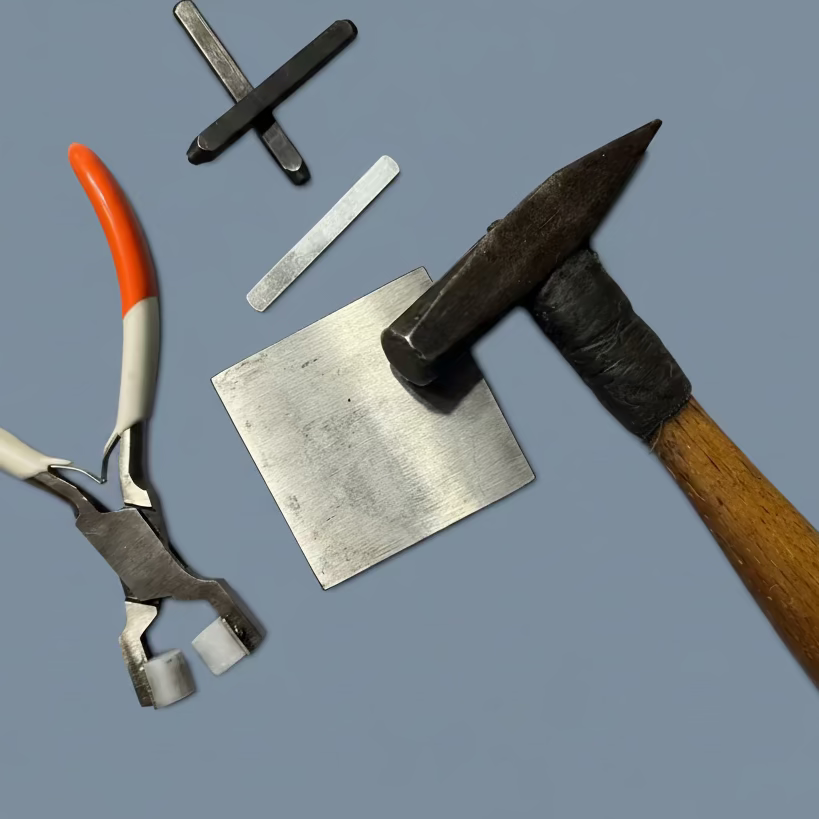 Set of tools used by Griffon for hand stamping includes a hammer, pliers, and metal pieces on a gray background
