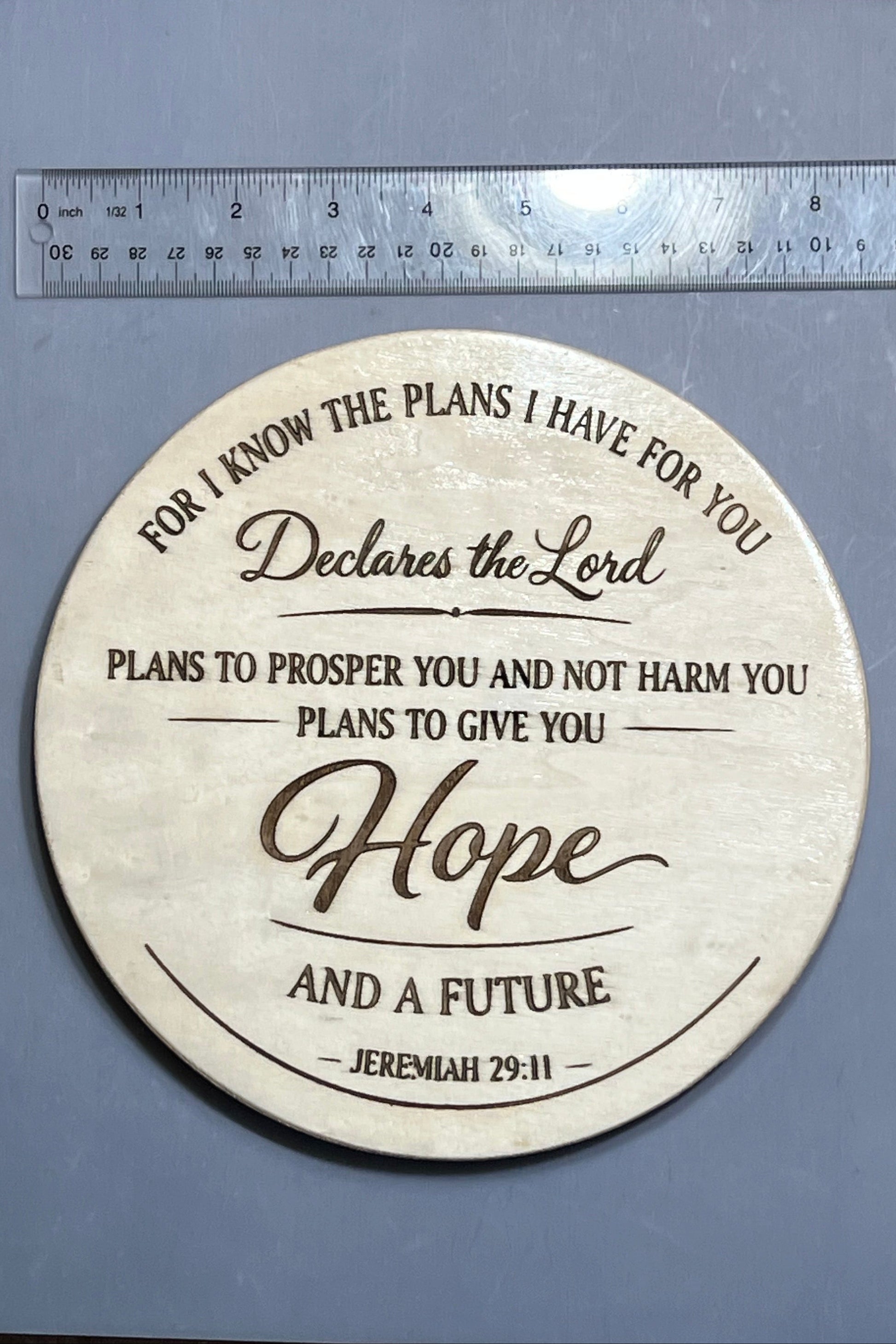 Round wooden plaque with engraved text with a ruler for scale.