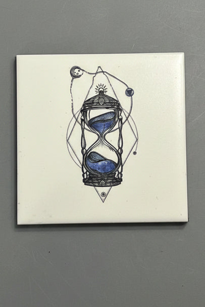 A square ceramic tile plaque featuring a black line art illustration of an hourglass with blue sand. 