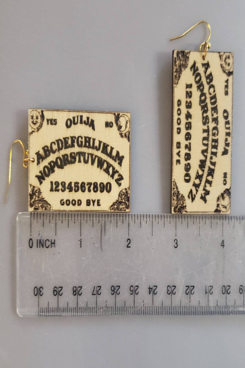 Ouija board earrings with a ruler for scale on a gray background