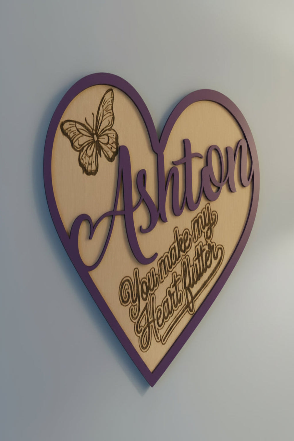 Heart-shaped decorative sign showing the name 'Ashton' and a butterfly design with the slogan 'you make my heart flutter' on a raw wood background