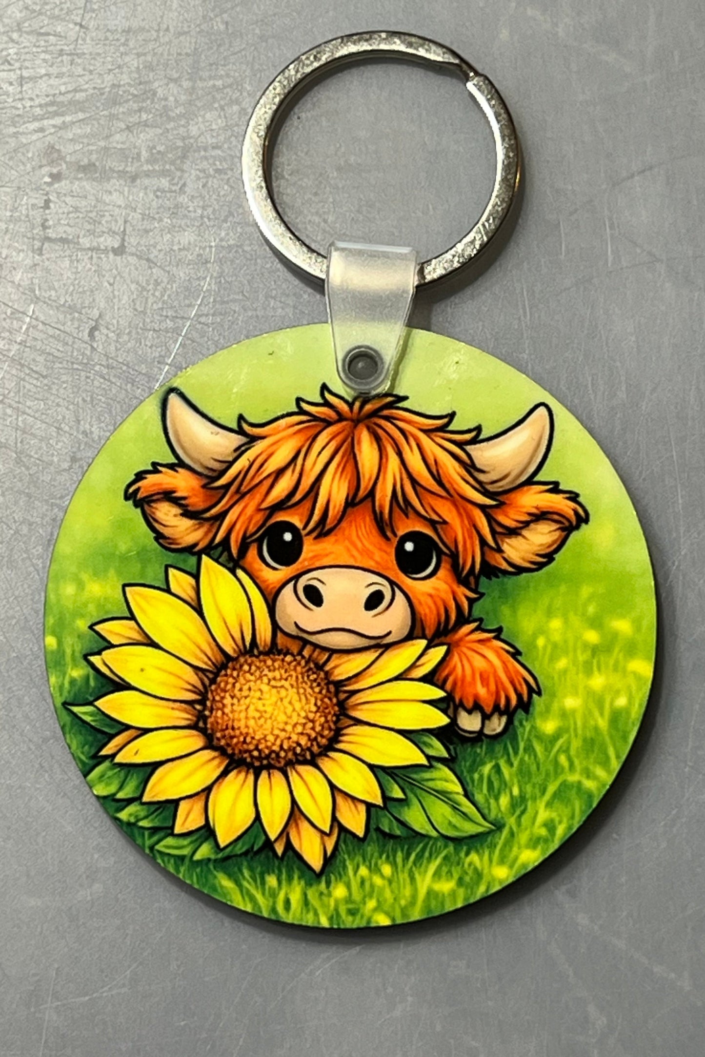 Round Keychain with a cartoon image of a highland cow looking over a sunflower