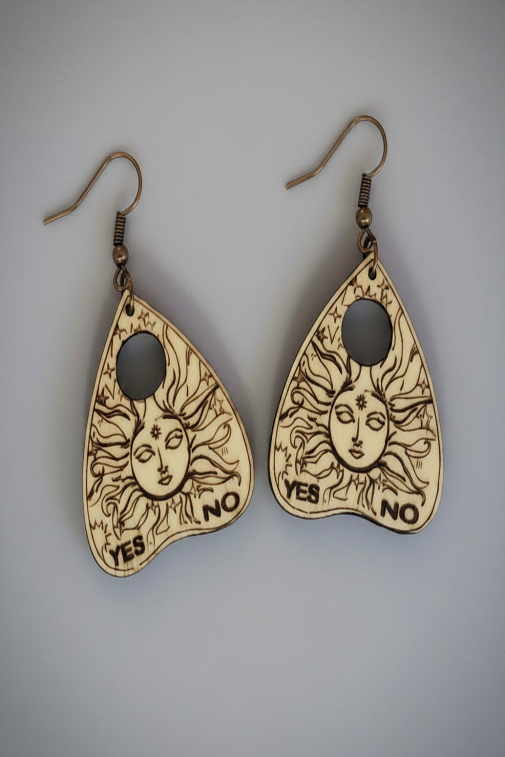Pair of wooden planchette earrings with sun designs and 'YES'/'NO' etched in wood  on a light gray background