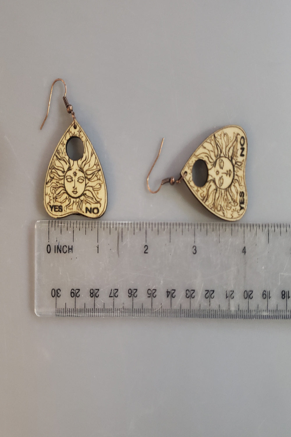 Yes No earrings with sun face design on a gray background with a ruler for scale.
