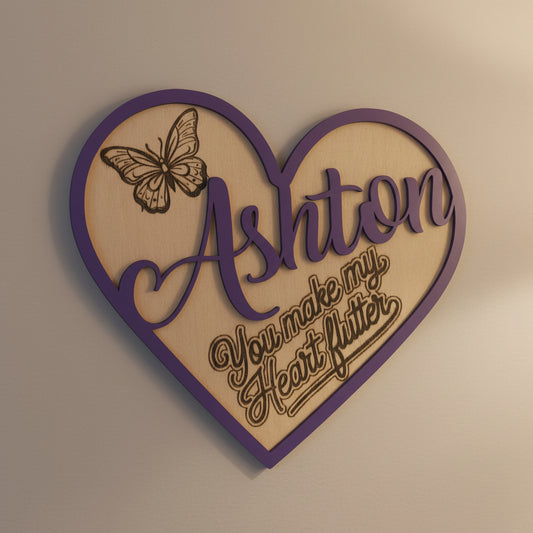 Heart-shaped decorative sign showing the name 'Ashton' and a butterfly design with the slogan 'you make my heart flutter' on a beige background
